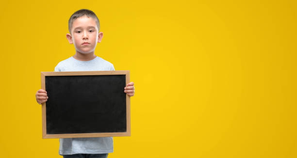 istock Dark haired little child holding a blackboard with a confident expression on smart face thinking serious 1044223344