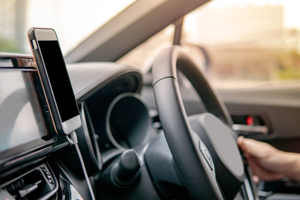istock Male driver hand holding on steering wheel using smartphone for GPS navigation. Mobile phone mounting with magnet on the car console in modern car. Urban driving lifestyle with mobile app technology 1044224100