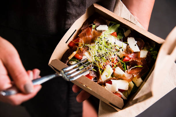 mano de mujer sostiene una ensalada fresca lejos de tomar en una caja de almuerzo. - comida para llevar fotos fotografías e imágenes de stock