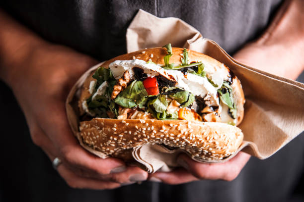 mujer es la celebración de una hamburguesa fresco bagel antes de comer. - hamburguesa alimento fotografías e imágenes de stock