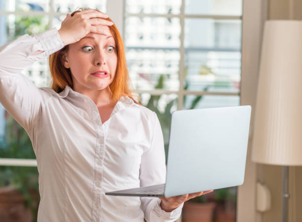 istock Redhead woman using computer laptop at home stressed with hand on head, shocked with shame and surprise face, angry and frustrated. Fear and upset for mistake. 1044227832