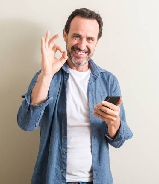 istock Senior man using smartphone doing ok sign with fingers, excellent symbol 1044246048