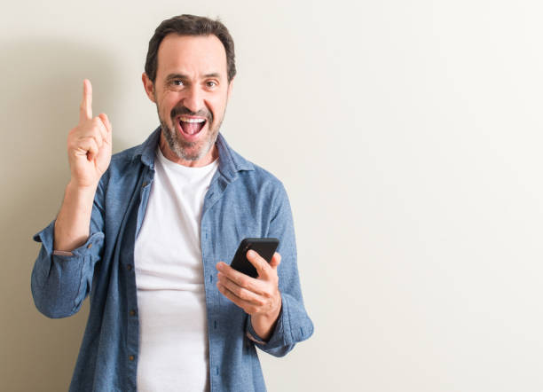 istock Senior man using smartphone surprised with an idea or question pointing finger with happy face, number one 1044246164