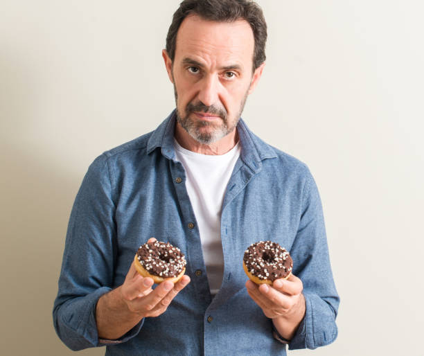 istock Senior man eating chocolate donut with a confident expression on smart face thinking serious 1044247396