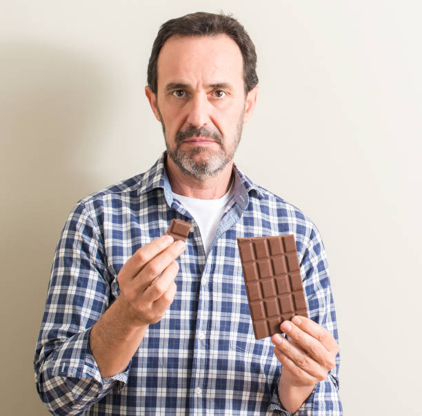 istock Senior man eating chocolate bar with a confident expression on smart face thinking serious 1044247826