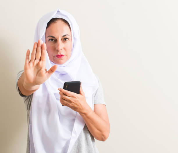 istock Arabian woman using smartphone with open hand doing stop sign with serious and confident expression, defense gesture 1044248430