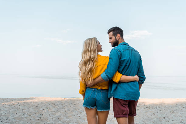 istock back view of couple hugging, walking and looking at each other on beach 1044248514