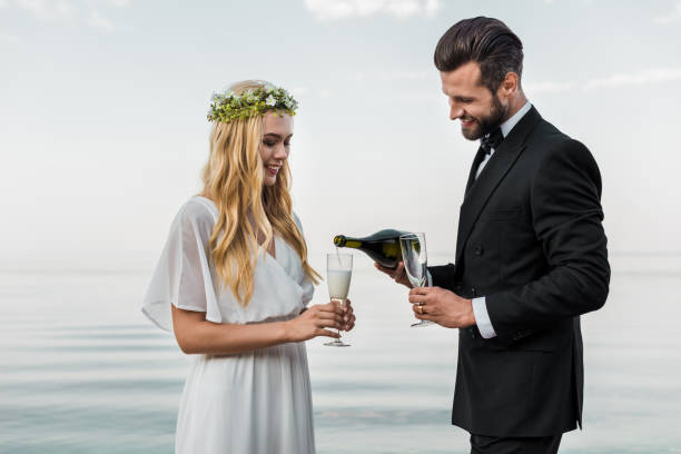 handsome groom pouring champagne into glasses on beach