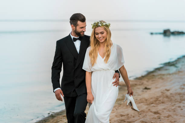 istock affectionate wedding couple hugging and walking on beach, bride holding high heels in hand 1044249240
