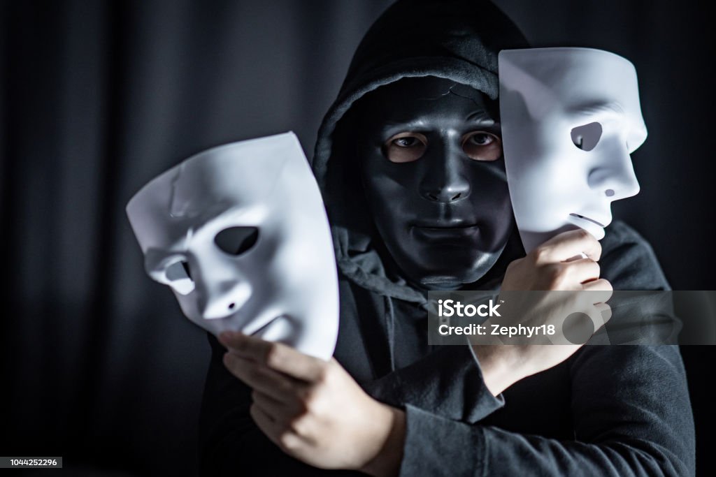 Mystery Hoody Man Wearing Black Mask Holding Two White Masks In