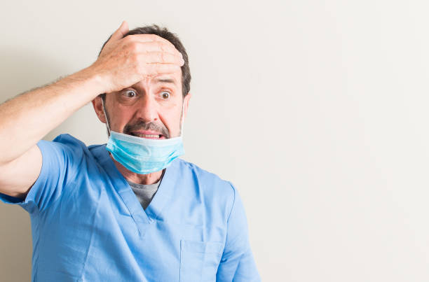 Senior doctor man using mask stressed with hand on head, shocked with shame and surprise face, angry and frustrated. Fear and upset for mistake. Senior doctor man using mask stressed with hand on head, shocked with shame and surprise face, angry and frustrated. Fear and upset for mistake. oops stock pictures, royalty-free photos & images