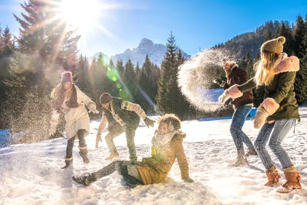 Women and men having snowball fight in snow on sunny day.