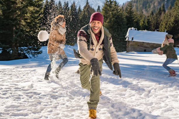 Man laughing and throwing snowball into air while having fun outside with his friends.