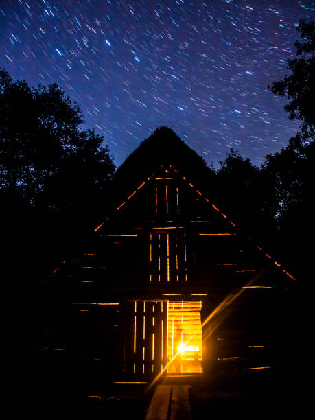 istock Old cabin in the woods lighted from inside with candles under stars 1044254530