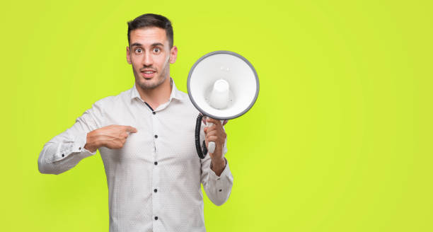 istock Handsome young man holding microphone with surprise face pointing finger to himself 1044257312