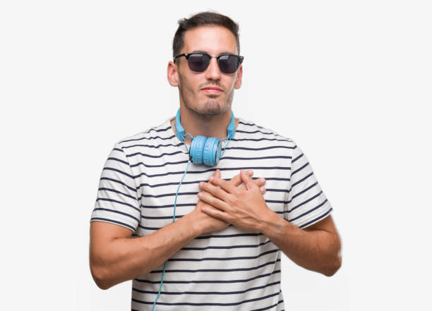 笑みを浮かべてヘッドフォンを身に着けているハンサムな若い男は、目を閉じてと感謝のジェスチャーの顔に胸に手します。健康の概念。 - natural pattern audio ストックフォトと画像