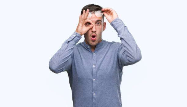 istock Handsome young elegant man wearing glasses doing ok gesture shocked with surprised face, eye looking through fingers. Unbelieving expression. 1044257920