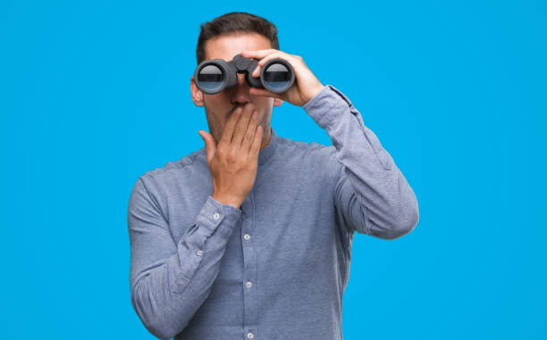 istock Handsome young man looking through binoculars cover mouth with hand shocked with shame for mistake, expression of fear, scared in silence, secret concept 1044258220