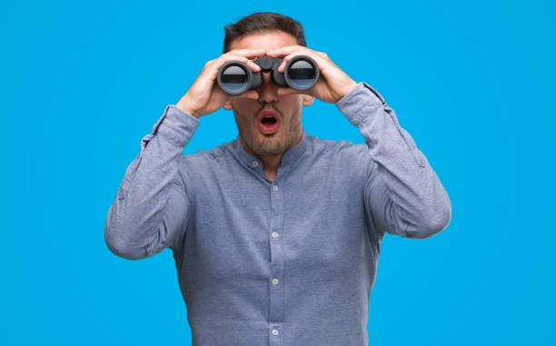 istock Handsome young man looking through binoculars scared in shock with a surprise face, afraid and excited with fear expression 1044258230