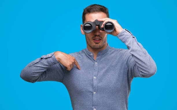 istock Handsome young man looking through binoculars with surprise face pointing finger to himself 1044258234