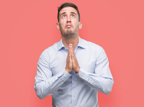 istock Handsome young businessman begging and praying with hands together with hope expression on face very emotional and worried. Asking for forgiveness. Religion concept. 1044259434