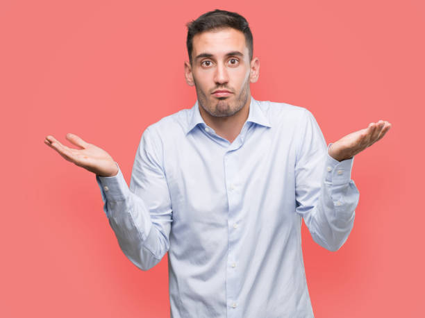 istock Handsome young businessman clueless and confused expression with arms and hands raised. Doubt concept. 1044259534