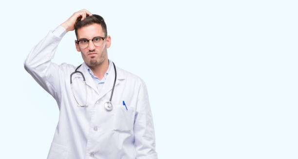 istock Handsome young doctor man confuse and wonder about question. Uncertain with doubt, thinking with hand on head. Pensive concept. 1044262528