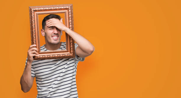 istock Handsome young man looking through vintage art frame stressed with hand on head, shocked with shame and surprise face, angry and frustrated. Fear and upset for mistake. 1044262764