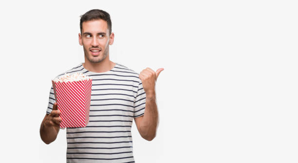 istock Handsome young man eating popcorn pointing with hand and finger up with happy face smiling 1044262918