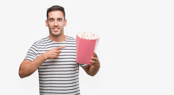 istock Handsome young man eating popcorn very happy pointing with hand and finger 1044263030