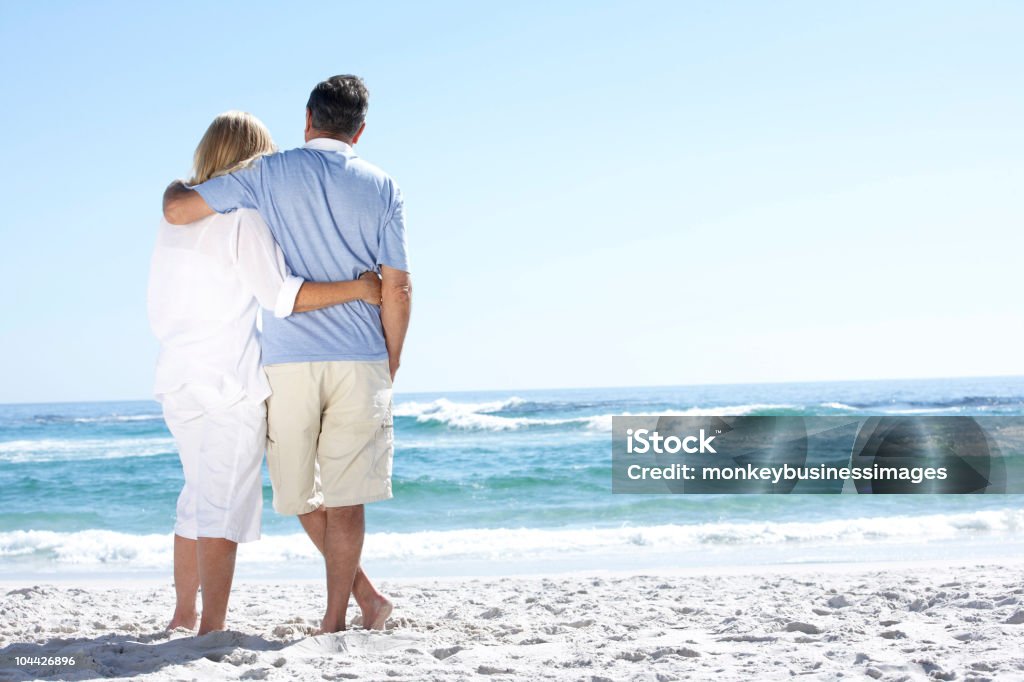 Casal de idosos caminhando ao longo da praia com vista para o mar - Foto de stock de 60 Anos royalty-free