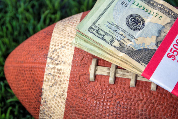 money on football close up of wrapped money stack on football and green grass background sports betting stock pictures, royalty-free photos & images