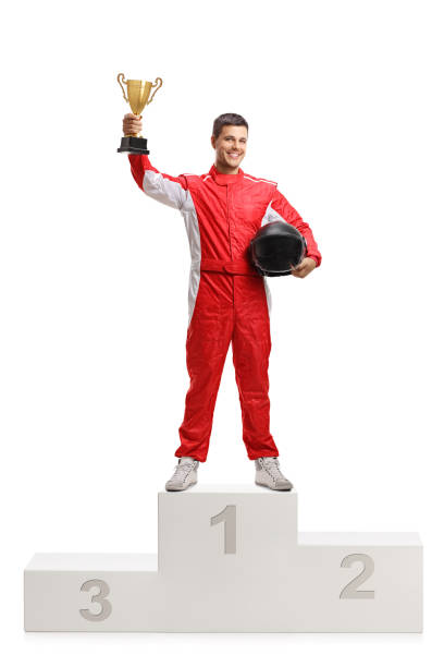 Male racer winner on a winner's pedestal with a gold trophy cup Full length portrait of a male racer winner on a winner's pedestal with a gold trophy cup isolated on white background winners podium photos stock pictures, royalty-free photos & images
