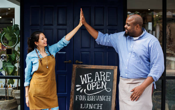 Cheerful business owners standing with open blackboard Cheerful business owners standing with open blackboard small business owner stock pictures, royalty-free photos & images