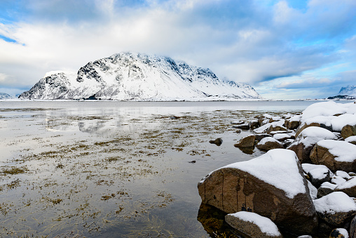 Sonwy winter landscape at the shore of Flakstadoya one of the islands of the Lofoten archipel in Norway The mountains are covered in snow and the village of Flakstad lies below the mountains.