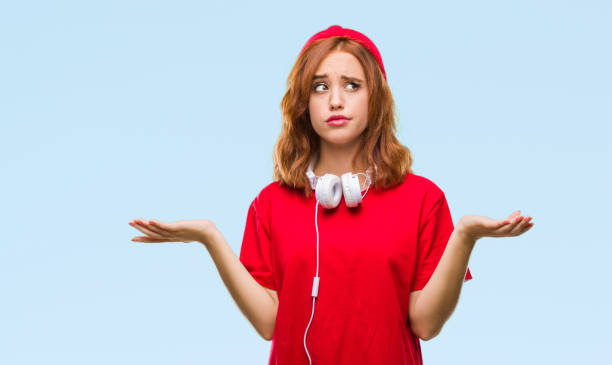 young beautiful hipster woman over isolated background wearing headphones and cap clueless and confused expression with arms and hands raised. doubt concept. - head and shoulders audio imagens e fotografias de stock