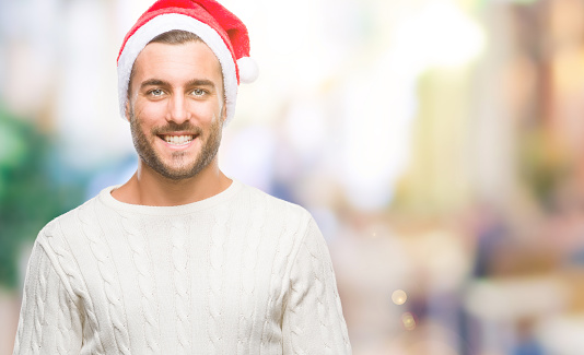Young handsome man wearing santa claus hat over isolated background with a happy and cool smile on face. Lucky person.