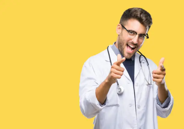Photo of Young handsome doctor man over isolated background pointing fingers to camera with happy and funny face. Good energy and vibes.