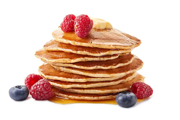 Stack of pancakes with maple syrup and fresh berries isolated on white background