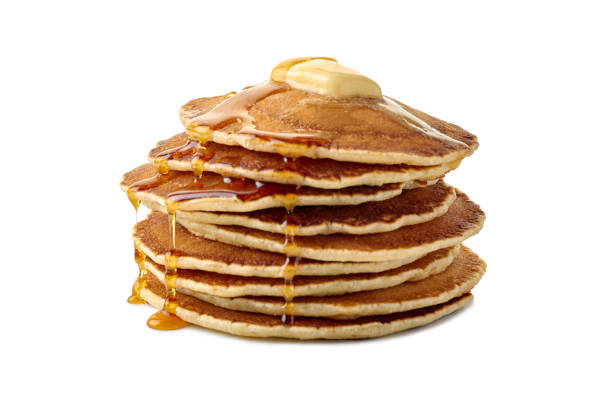 Stack of pancakes with butter and a flowing maple syrup on white
