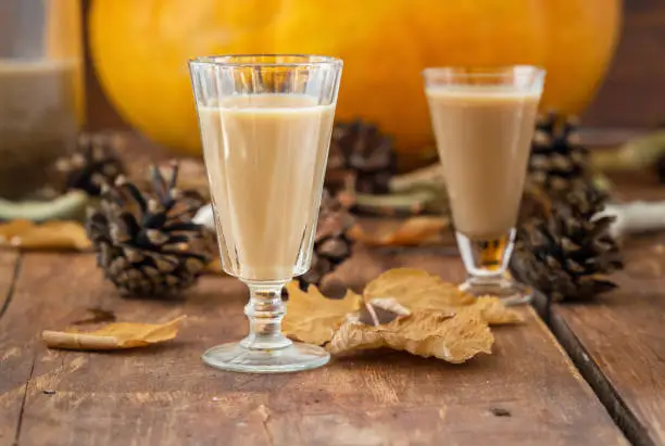 Homemade milk liqueur in glass from pumpkin, autumn drink holiday. Dry leaves