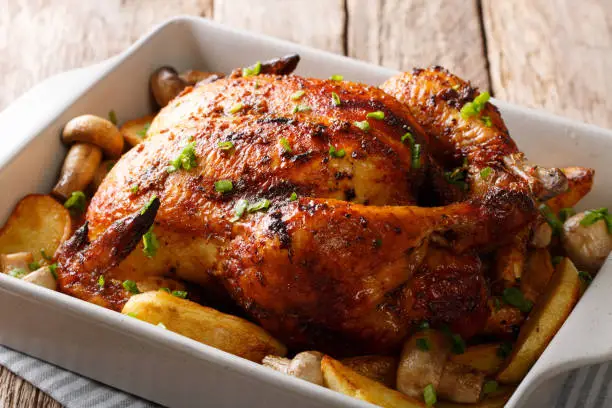 Whole grilled chicken with mushrooms and potatoes close-up in a baking dish. horizontal