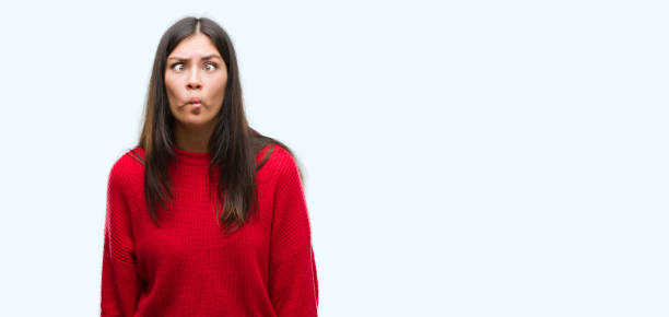 istock Young beautiful hispanic wearing red sweater making fish face with lips, crazy and comical gesture. Funny expression. 1044335346