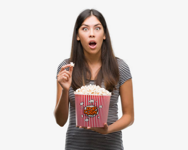 istock Young beautiful hispanic eating popcorn scared in shock with a surprise face, afraid and excited with fear expression 1044335622