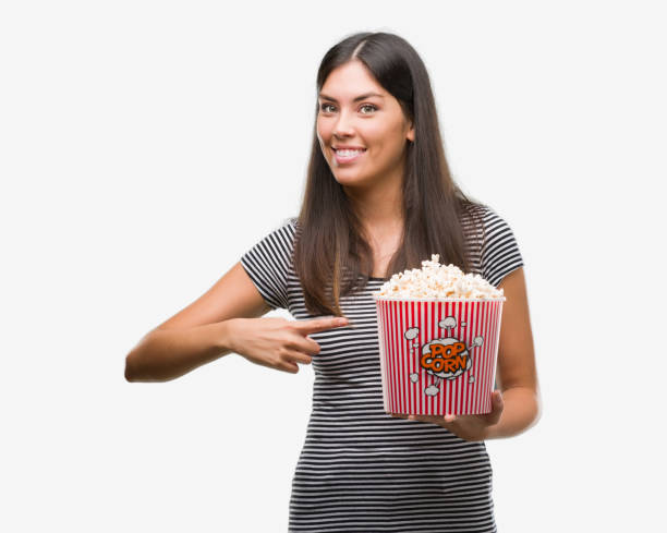 istock Young beautiful hispanic eating popcorn very happy pointing with hand and finger 1044335670