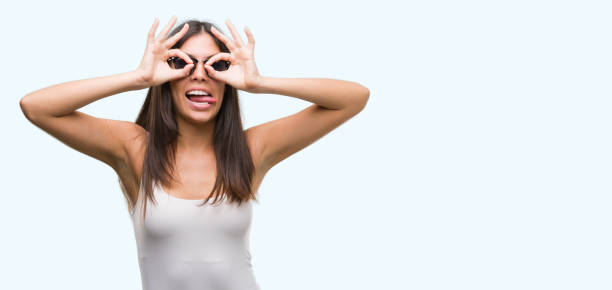 istock Young beautiful hispanic wearing sunglasses doing ok gesture like binoculars sticking tongue out, eyes looking through fingers. Crazy expression. 1044336056