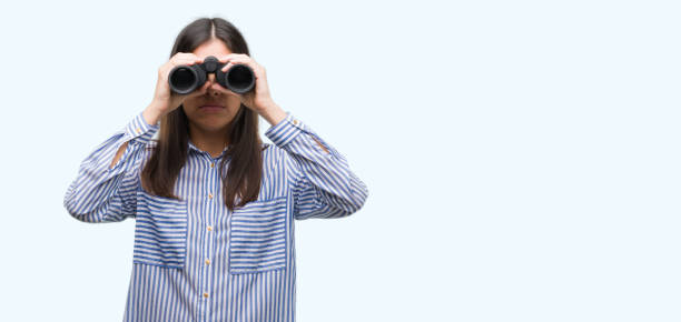 istock Young hispanic woman holding binoculars with a confident expression on smart face thinking serious 1044340444