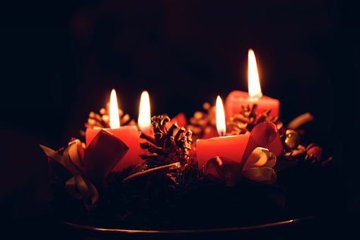Low light Christmas Advent wreath with burning red candles on black background