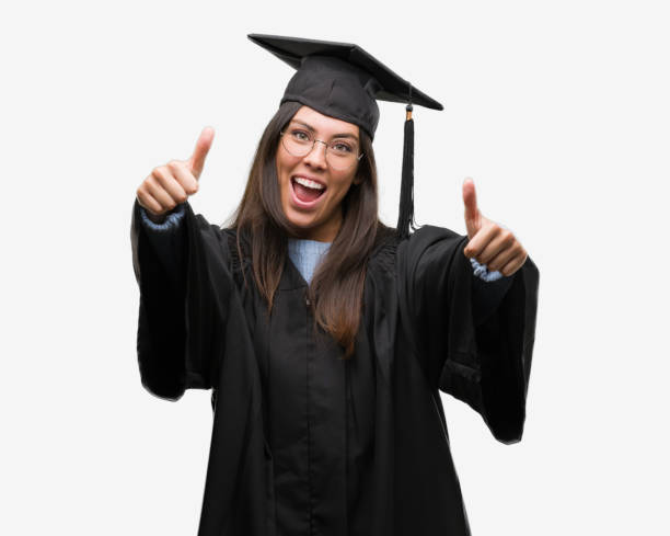 istock Young hispanic woman wearing graduated cap and uniform approving doing positive gesture with hand, thumbs up smiling and happy for success. Looking at the camera, winner gesture. 1044343376