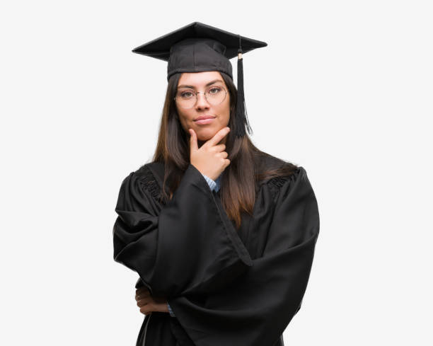 istock Young hispanic woman wearing graduated cap and uniform looking confident at the camera with smile with crossed arms and hand raised on chin. Thinking positive. 1044343430